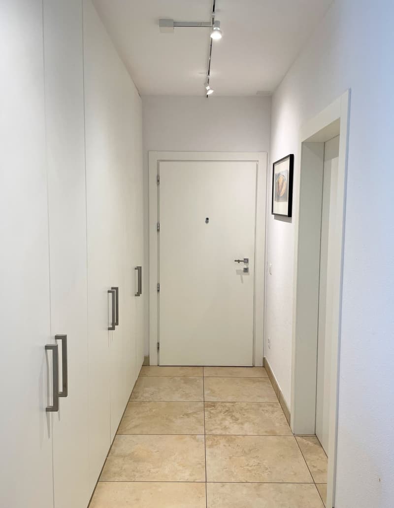An empty corridor with a white door, two closets, a picture frame on the wall, and tiled flooring.