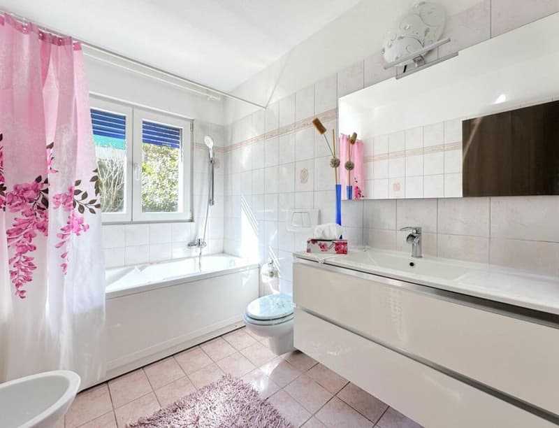 Bathtub, toilet, double sink, mirror, shower head, flower curtains, rug, window with blinds