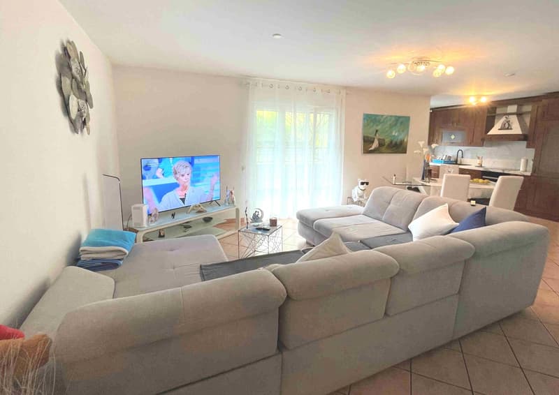 white walls, light brown tiled floor, grey sofa, side table, TV, decorative wall art, window with white curtains