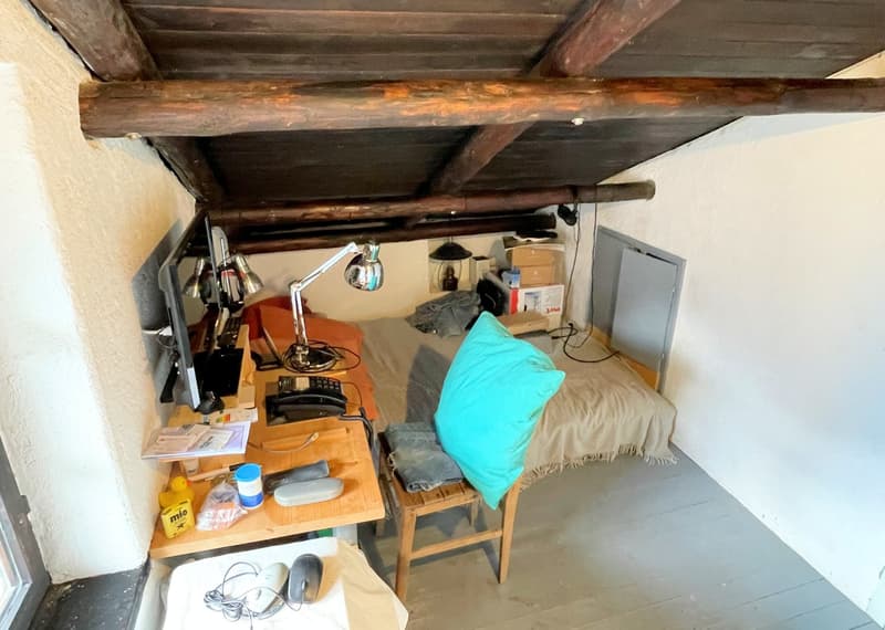small attic room, bed, desk, lamp, computer monitor, cushioned chair, wooden beams, gray floor