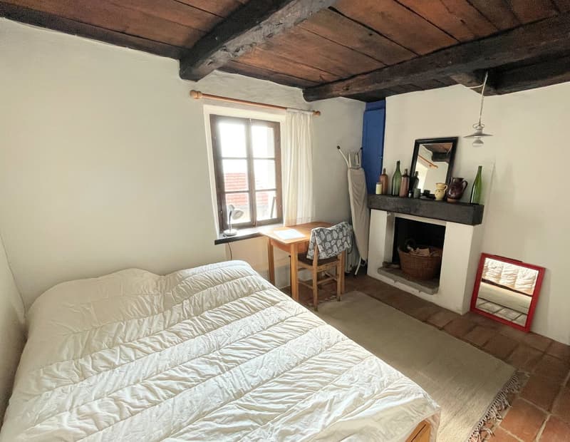 A single bed, a wooden desk with a chair, a fireplace, a lamp on the desk, a mirror and some storage bottles on a shelf.