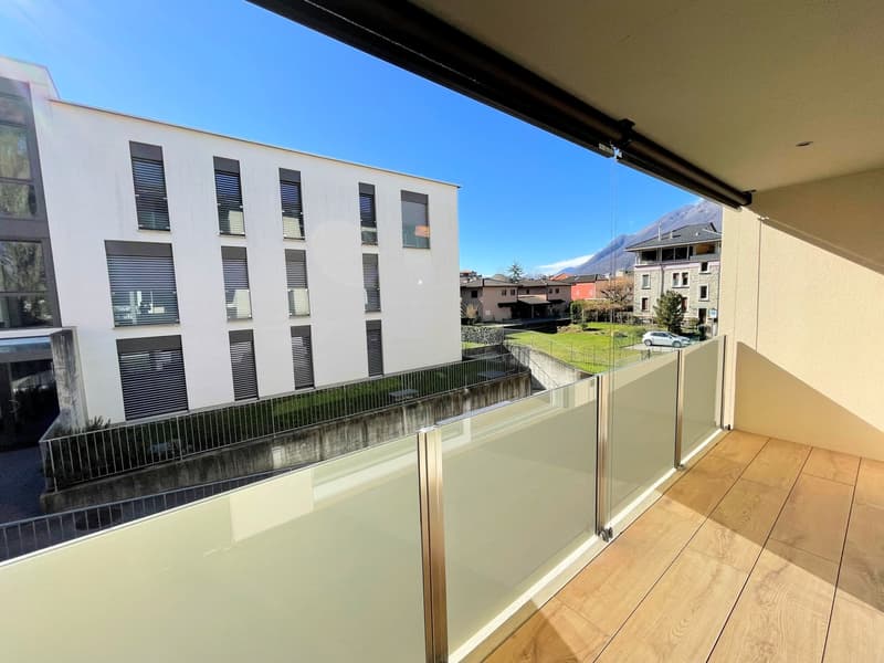 Modern balcony with glass railing, wooden floor, clear sky view