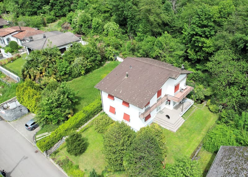 Two story house, white walls, brown roof, 4 windows, balcony, driveway, stone steps, car parked, grass garden