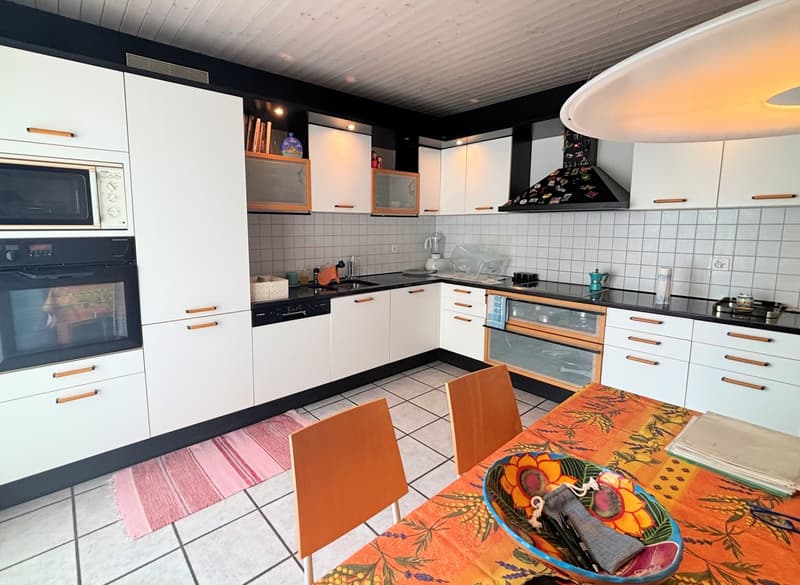 Modern kitchen with white cabinets, tiled floor, microwave, oven, dishwasher, dining table with chairs