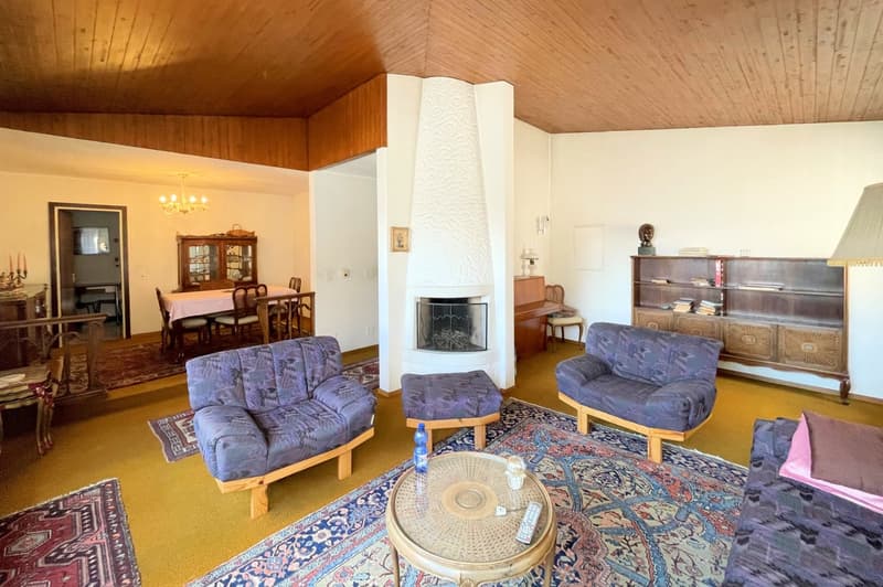 living room with blue sofas, round coffee table, dining area with table, chairs and cabinet, wooden ceiling, fireplace