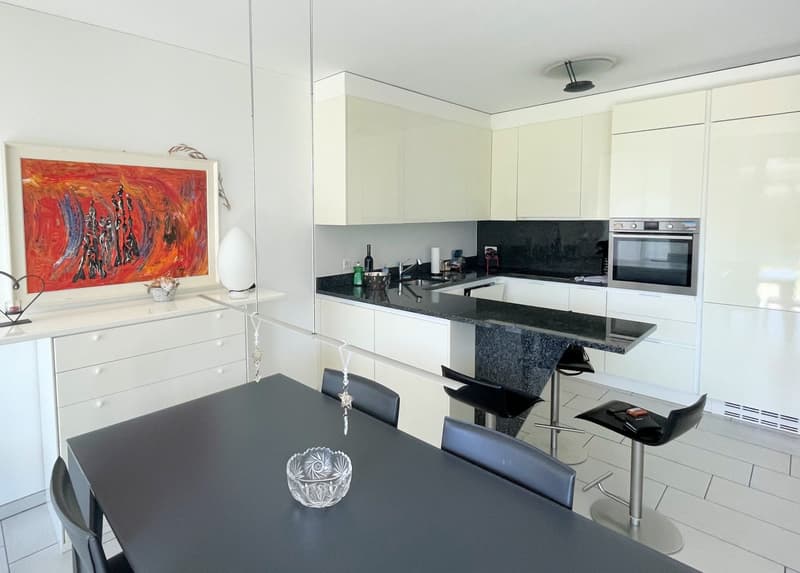 modern kitchen with dining area, white cabinets, black countertops, stainless steel appliances, dining table, black chairs, artwork on wall