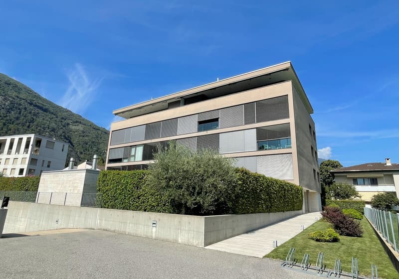 Modern apartment building, beige exterior, large windows, concrete wall, hedge, driveway, mountain view