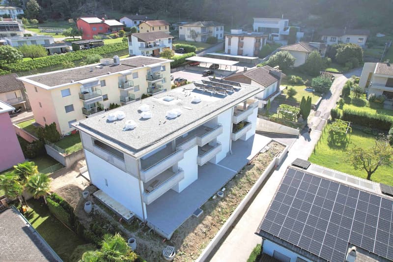 Aerial view of a residential building with multiple balconies, solar panels on the roof, and a car parking area.