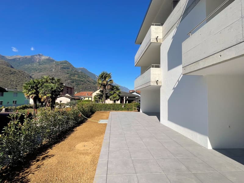 modern building with balconies, tiled walkway, greenery, mountains in the background