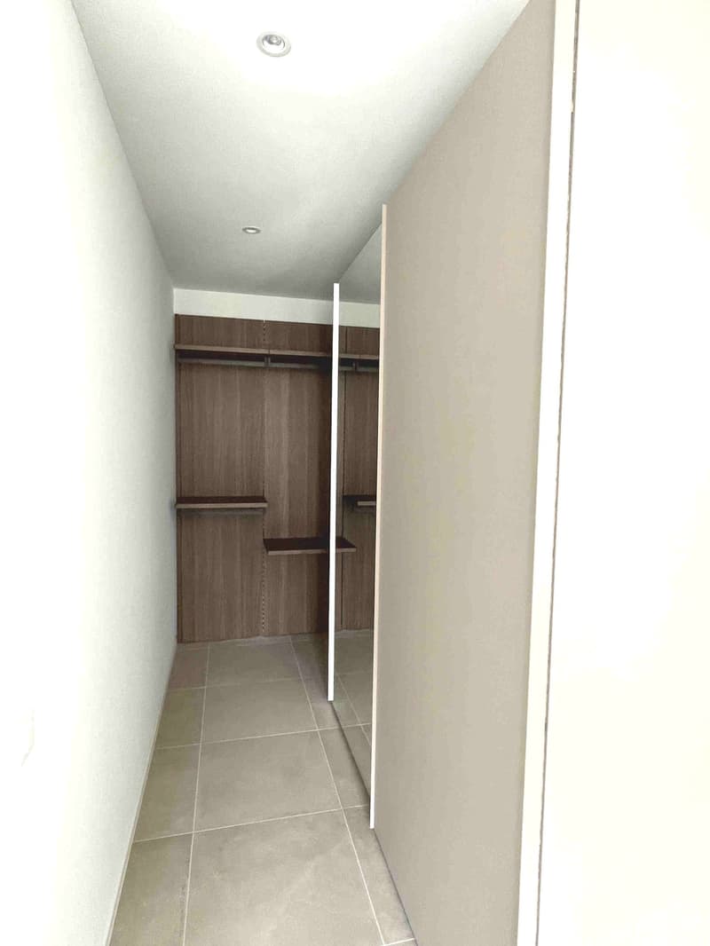 Empty room with tiled floor, white walls, wooden closet with shelves, mirror on the door