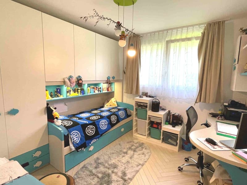 A child's bedroom with a bed, shelves, desk, chair, rug, and toys