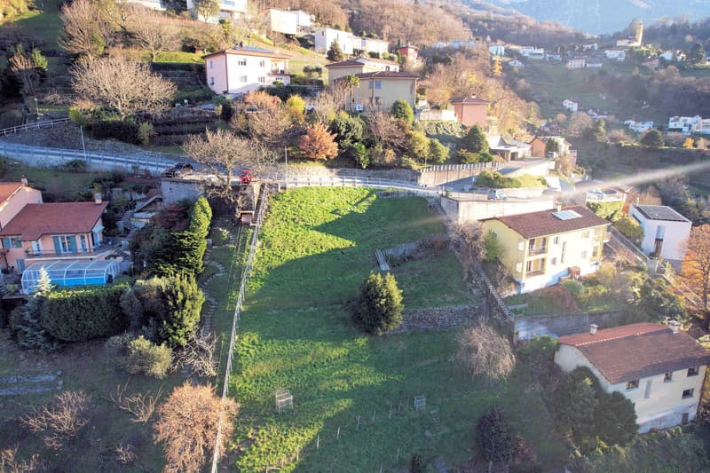 Aerial view of a hillside neighborhood with several houses, a large grassy field, and a road.