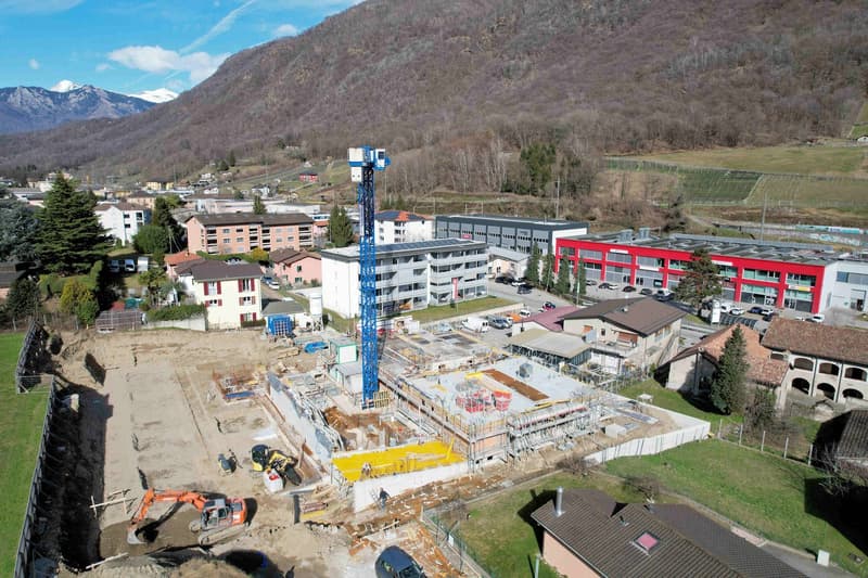 Construction site, multiple buildings, mountains in the background, cranes, machinery, ongoing construction