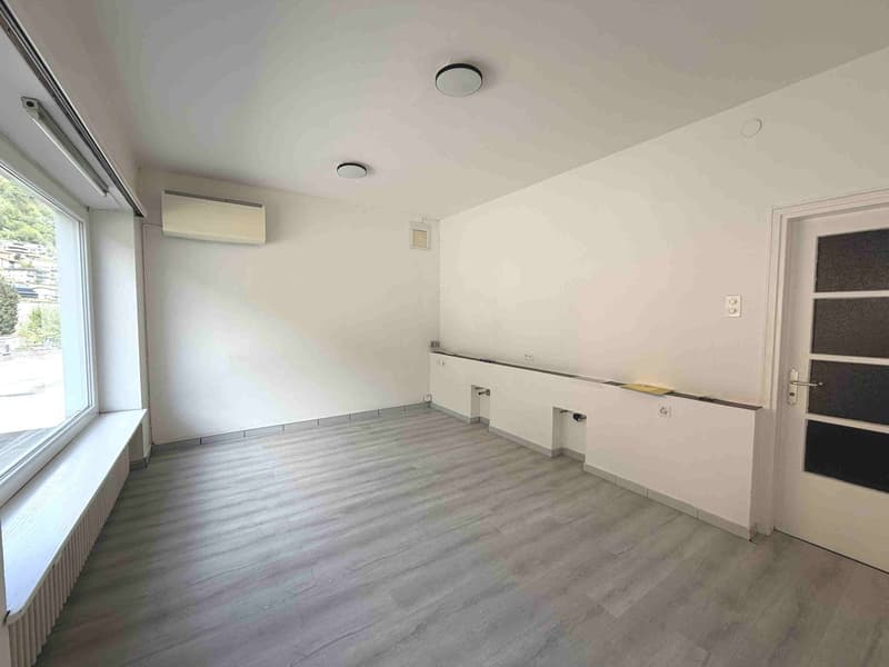 empty room, white walls, gray wooden floor, large window, built-in bench, air conditioning unit, power outlets, door