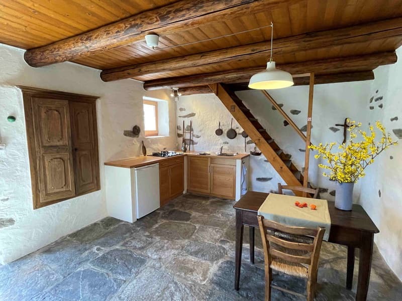 kitchen with dining area, wooden ceiling, stone floor, wooden cabinets, gas stove, sink, table, chairs, flower vase