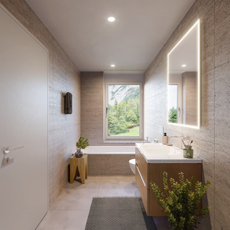 Bathroom features white walls and floors, bathtub, large mirror, wooden desk with potted plant, toilet, sink with faucet, faucet soap dispenser, wall mounted towel rack