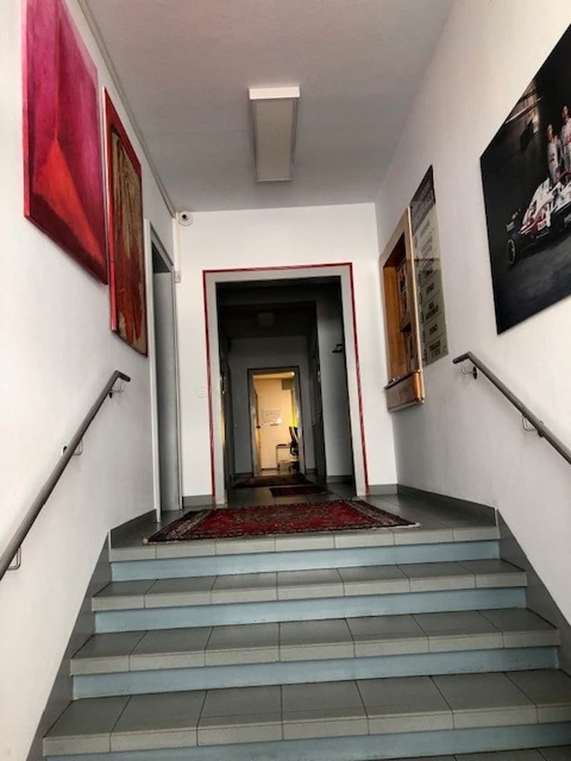 The image shows a hallway with a tiled floor, white walls, and a red painting on the wall. There is a doorway visible at the end of the hallway.
