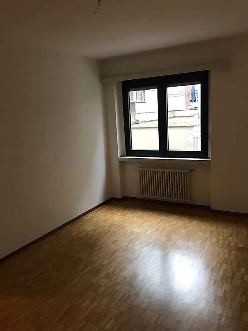 Empty room with wooden floors, white walls, a window with a white radiator below, and an outside view.