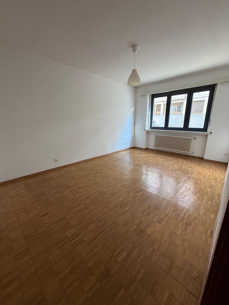 Empty room with white walls, wooden floor, windows with blinds, radiator.
