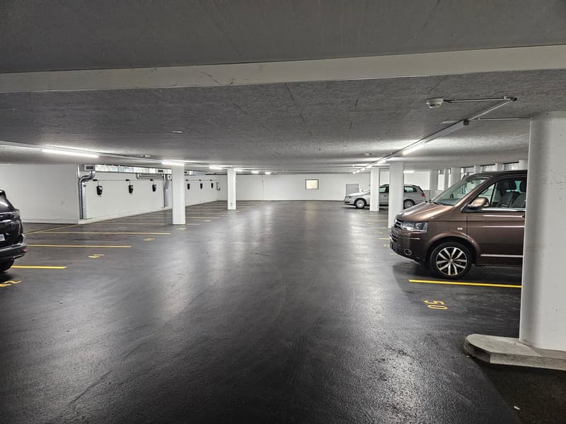 empty underground parking lot, concrete floor, parking stalls, 3 cars parked