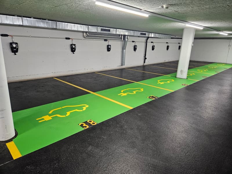 underground parking lot, green and yellow markings, chargers on the wall, 6 available parking spots