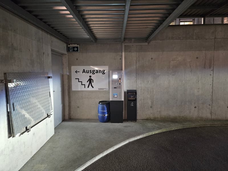 Underground parking space with a ticket machine, trash bin, and signage.