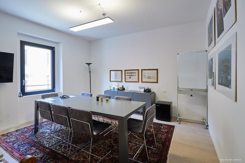Meeting room with desk, chairs, carpet, wall paintings, TV, lamp, whiteboard, storage cabinet, microwave