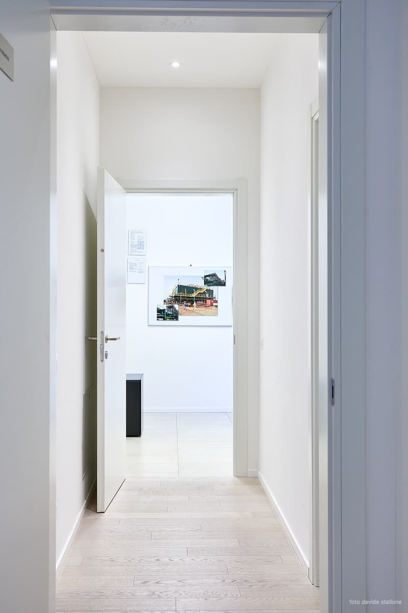 Open door leading to hallway, hardwood flooring, clean white walls, closed door at end of hallway