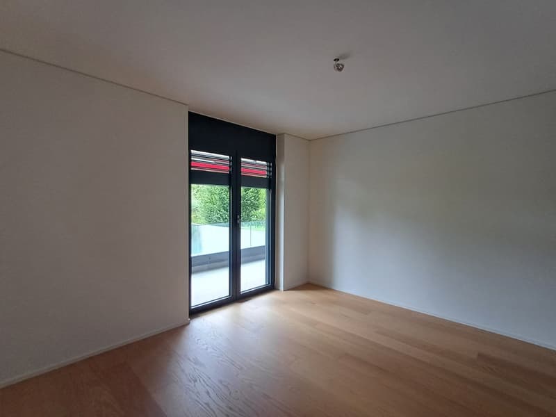 Empty room, white walls, wooden floor, sliding glass door leading to balcony, glass wall with red stripes on balcony