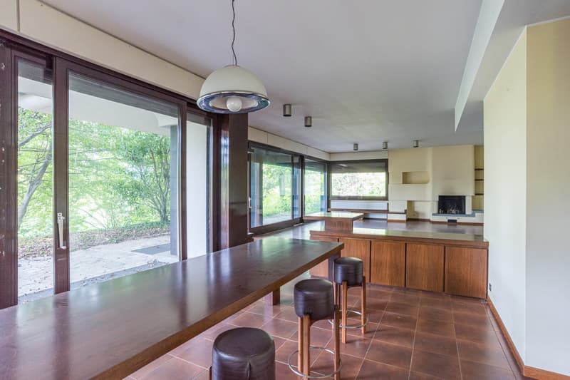 dining room with a long wooden table, four black stools, wooden flooring, glass door, glass windows, ceiling light