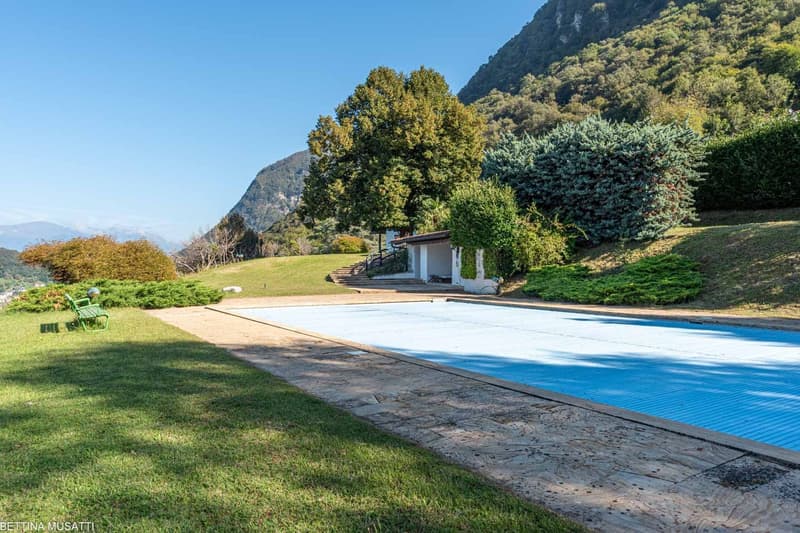 pool with concrete around, green benches, trees, bushes, grass, mountain