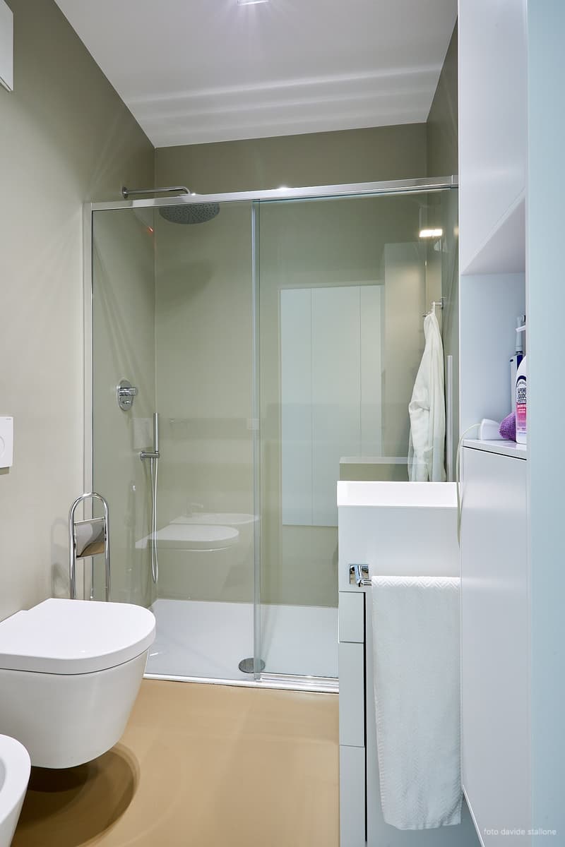 Modern bathroom with glass shower enclosure, white toilet, vanity cabinet, and towel rack.