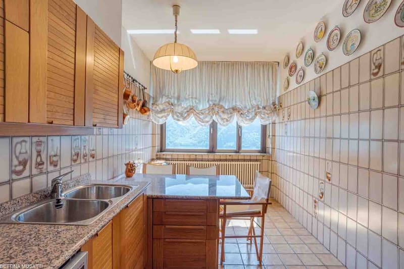Spacious kitchen with wooden cabinets, tiled walls, double sink, granite countertop, dining table, and decorative plates on the walls