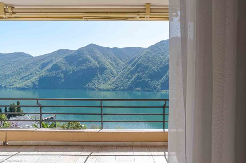 Spacious balcony with a stunning view of the mountainous landscape and a serene lake. The balcony features a metal railing and tiled flooring, providing an ideal spot to enjoy the scenic surroundings.