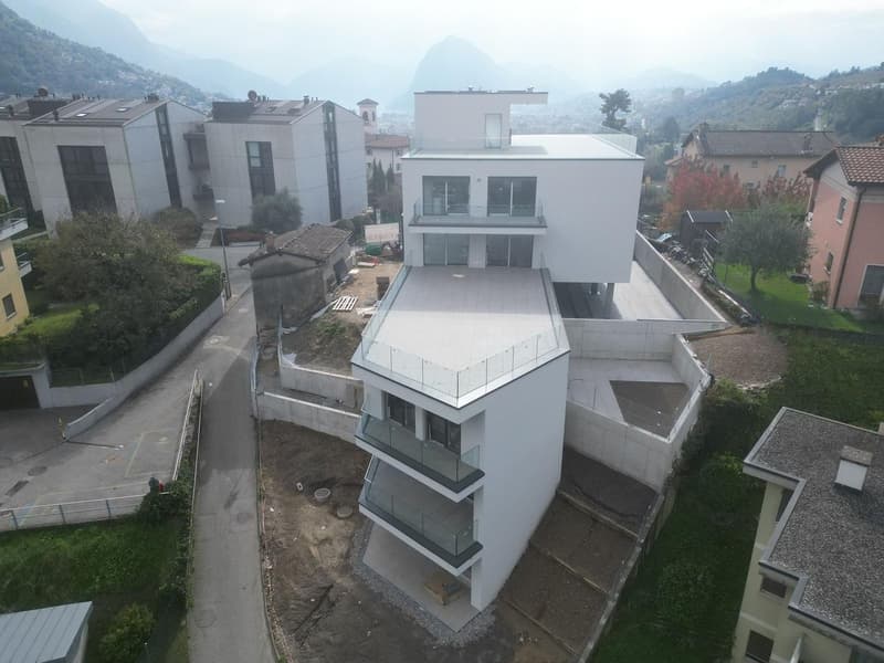 A multi-story white house with multiple glass balconies on an elevated plot with a sloped roof