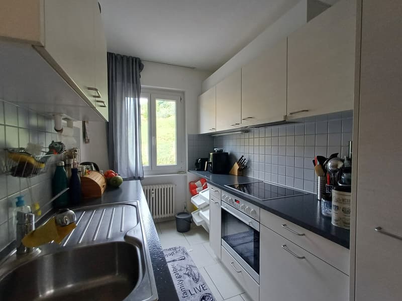 White cabinets, black countertops, stainless steel sink, gas stove, oven, kitchen utensils, radiator, window with curtain, tiled floor, white tiles