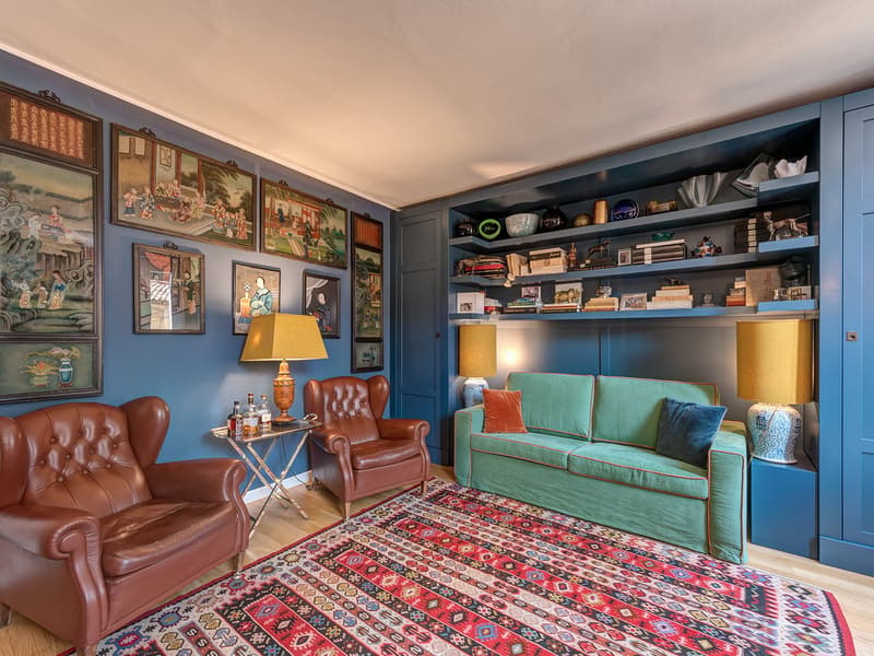 Living room with brown leather chairs, a green couch, a colorful carpet, side table, lamps, and a wooden floor