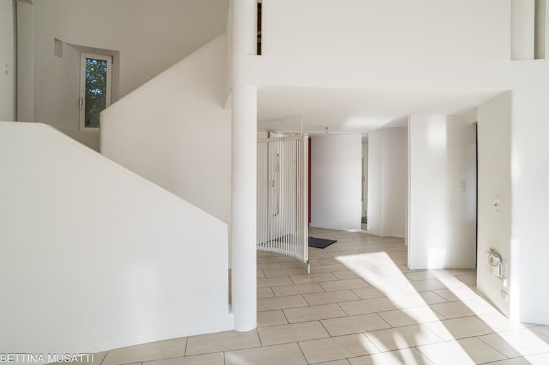 A corridor with white walls, tiled flooring, spiral staircase, white sliding gate, and a window.