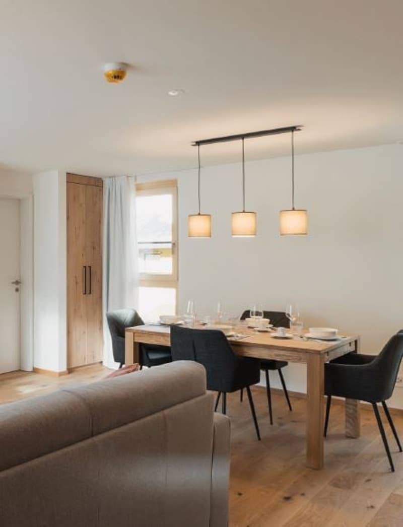 Dining room with wooden floor, white walls, wooden dining table, black chairs, table setting, lamps