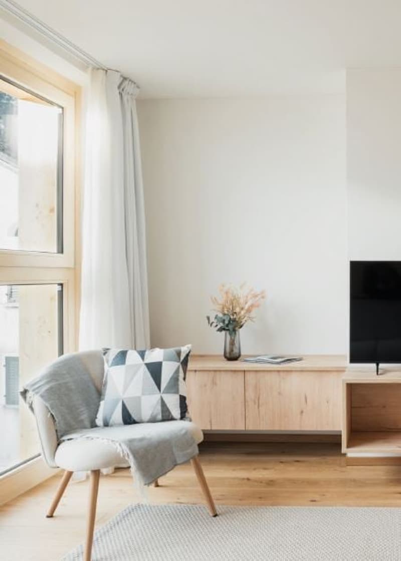 modern living room, neutral color palette, large windows, wooden floor, beige sofa, patterned pillow, wooden side table, TV, curtains