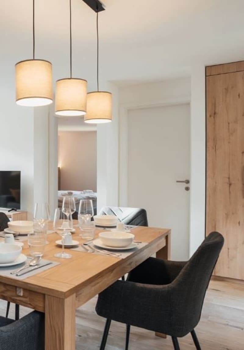 dining table, 4 chairs, white bowls, wine glasses, forks, knives, placemats, lamps, TV