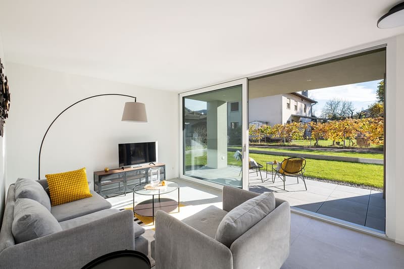 modern living room with gray couches, glass table, TV, floor lamp, sliding glass doors to terrace