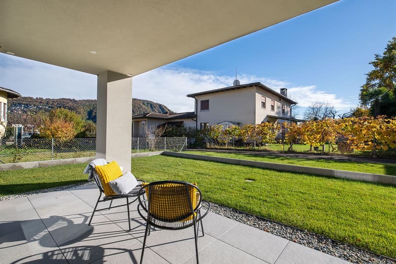 Terrace with chairs and cushions, green lawn, house in the background, mountains in the distance