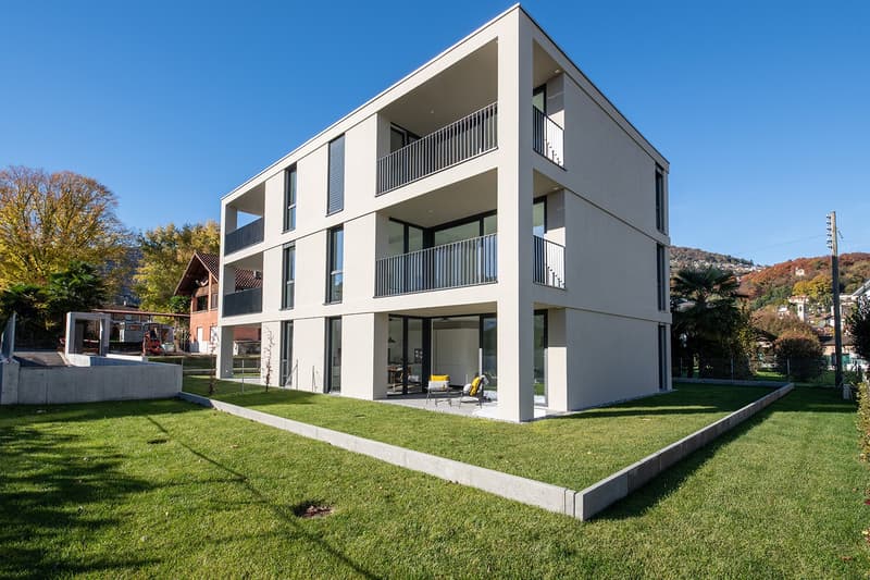 Modern 3-story house, white exterior, large windows, multiple balconies, concrete garden area