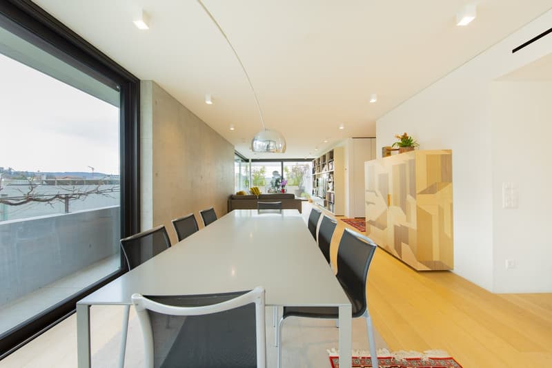 Dining room with a long table, chairs, large windows, and a balcony