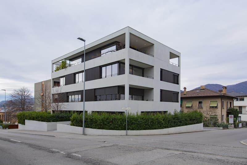 Modern white building with multiple balconies, concrete construction, multiple floors, surrounded by greenery