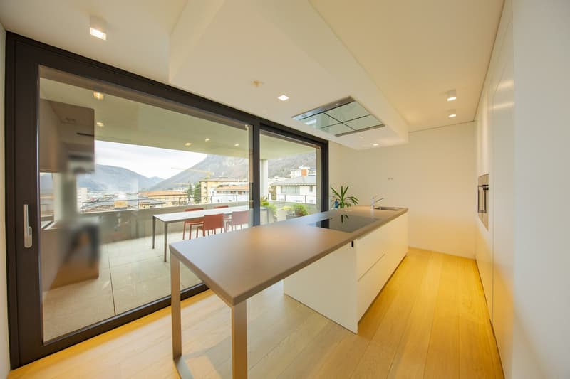 modern kitchen with large windows, wooden floor, island with sink and stove, balcony with table and chairs