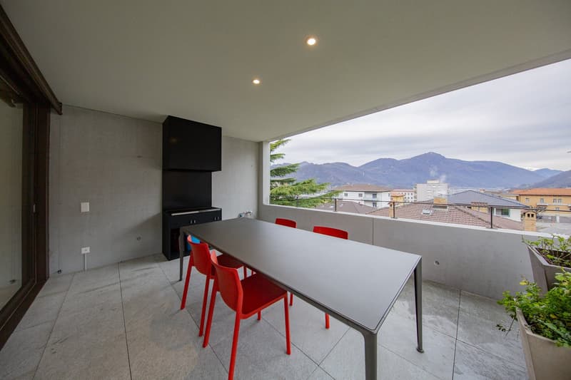 Balcony with table and chairs, concrete floor, concrete wall, potted plants, large window, mountains in the distance