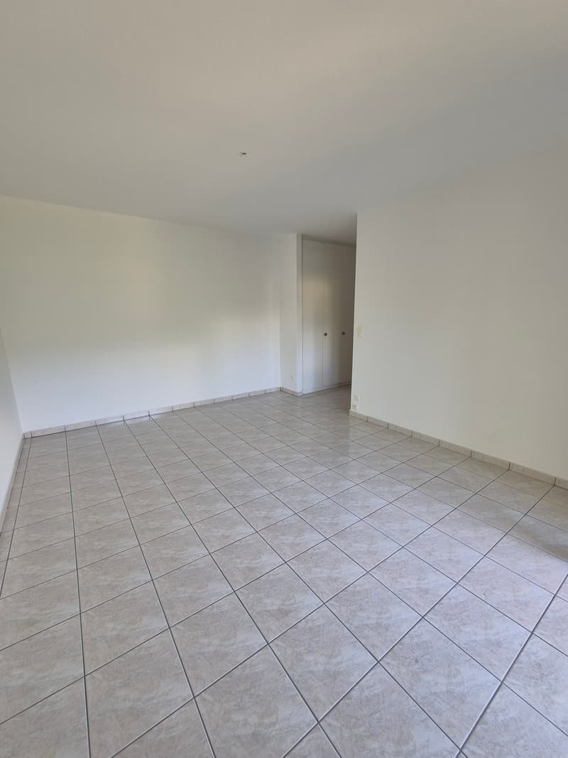 Empty room with white walls and gray tile flooring. The room appears to be a living room or bedroom with a doorway visible in the background.