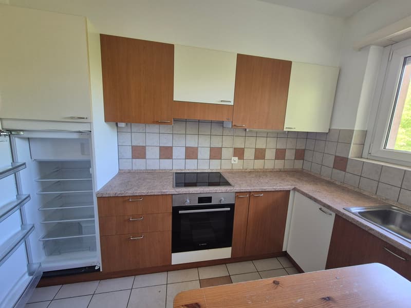 The image shows a kitchen with wooden cabinets, a tiled backsplash, a built-in oven, and a refrigerator. The countertop appears to be made of granite or a similar material. There is a dishwasher visible in the kitchen.